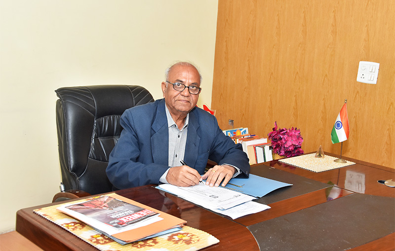 Man in a navy blazer signing papers at a desk with a small Indian flag.