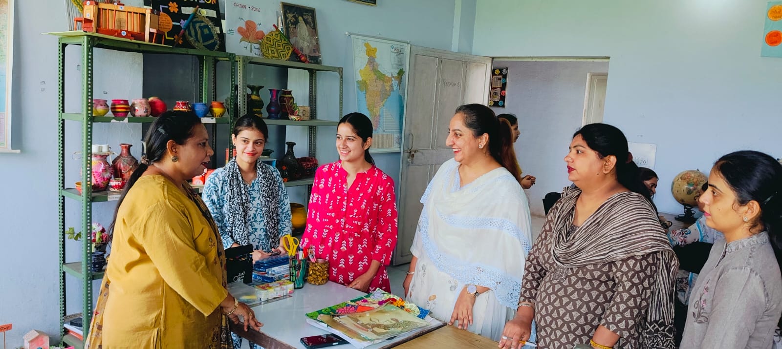 The art and craft room: a lecturer talks with students beside shelves of hand-painted pots and vases, a map of India on the wall behind.