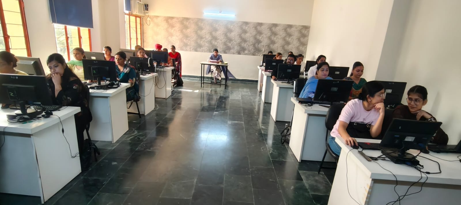 Students at work in the computer laboratory, seated at monitors along both sides of a polished stone floor.