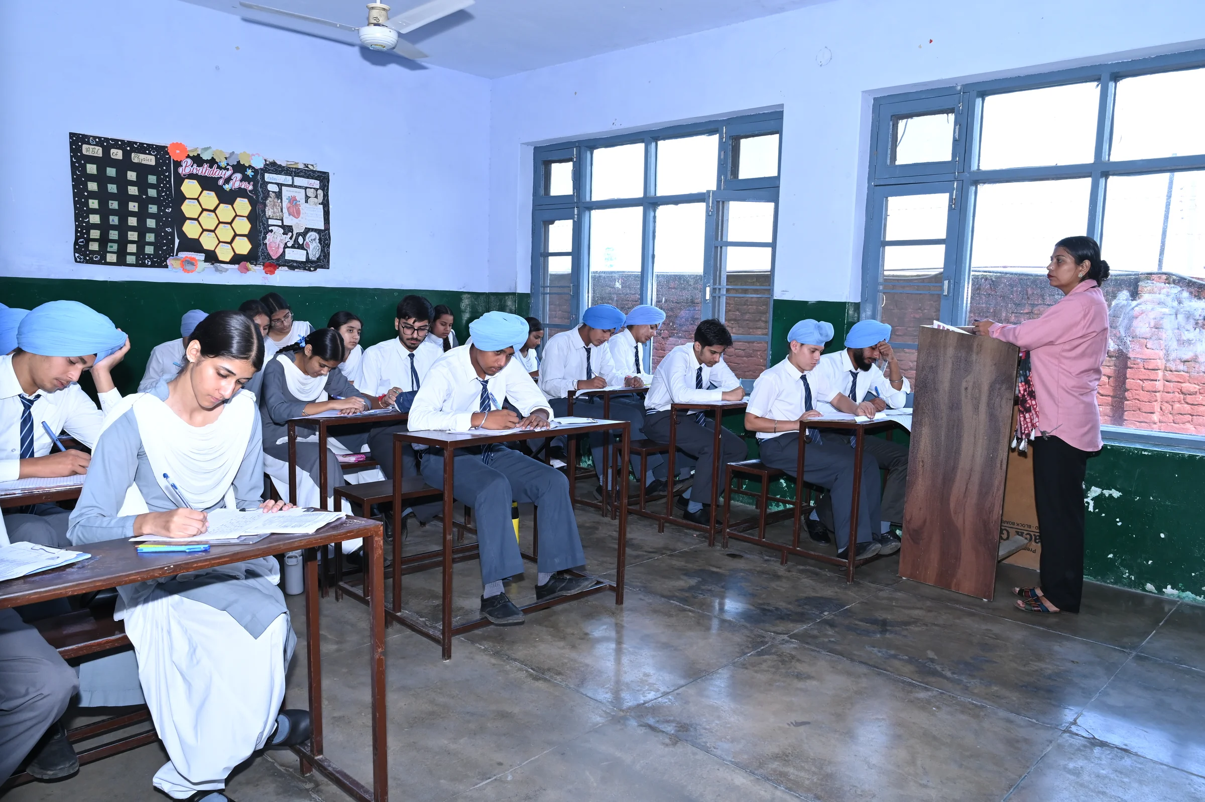 Senior students writing an examination in a classroom while a teacher supervises.