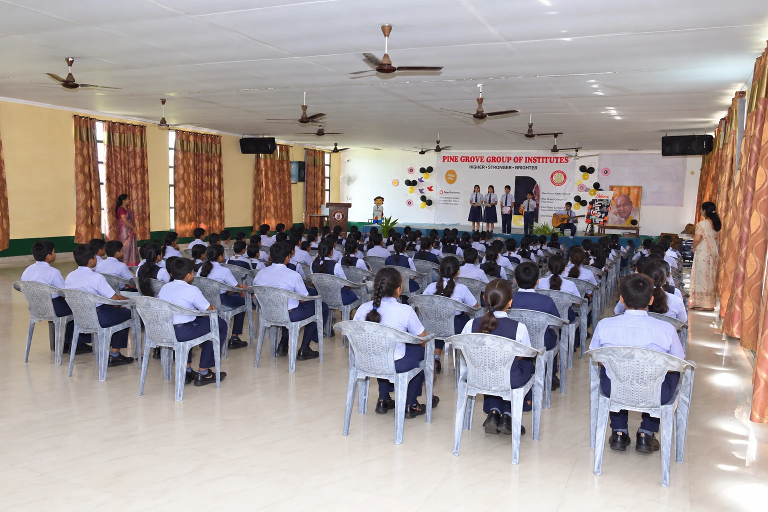 Illustrative visualization of a fictional student programme inside the real S. P. Kaushal Auditorium; not a photograph of an actual recorded event.